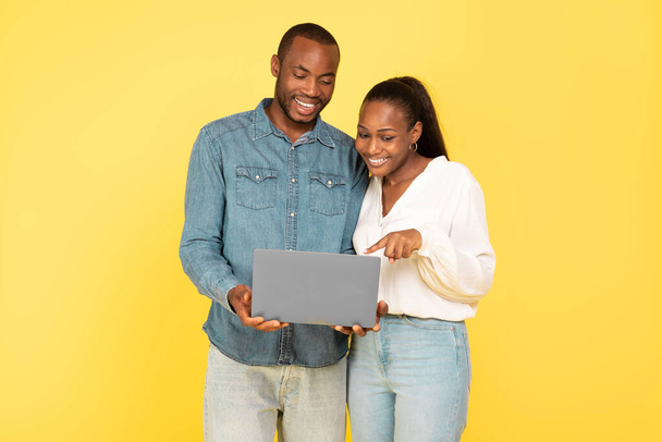 Mutlu siyah çift birlikte dizüstü bilgisayar kullanarak interneti tarıyor ve sarı stüdyonun arka planında çalışıyor. IT Teknoloji ve E-Öğrenme Konsepti - Fotoğraf, Görsel
