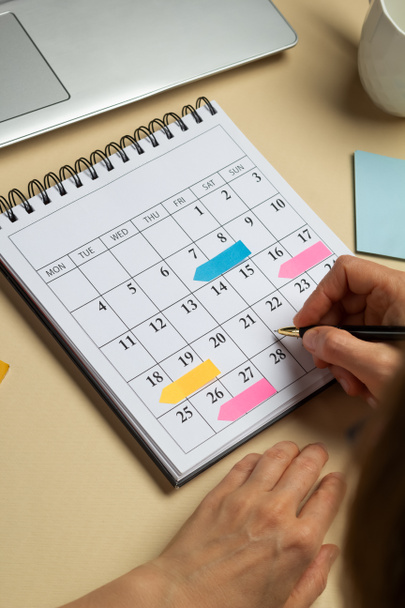 Χέρια μιας γυναίκας που σχεδιάζει και σηματοδοτεί τις ημερομηνίες του χρονοδιαγράμματος των επιχειρηματικών συναντήσεων στο ημερολόγιο. - Φωτογραφία, εικόνα