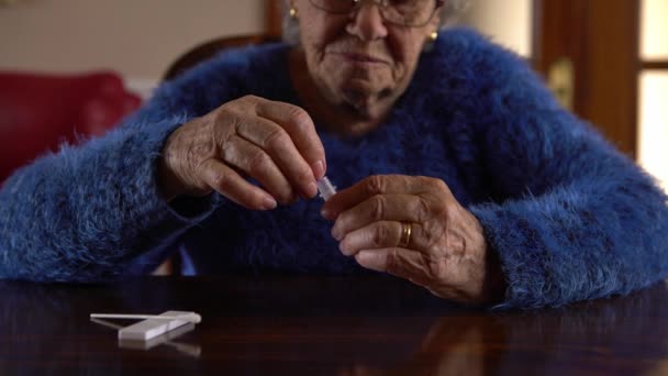 Белая старуха держит ватный тампон для носа, чтобы получить возможный положительный образец COVID-19 во время пандемии. Бабушка использует антиген процедуры на дому. - Кадры, видео