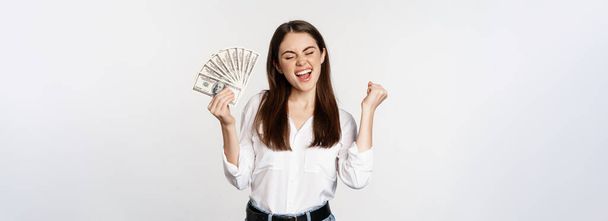 Joyful woman dancing with money, smiling pleased, winning prize, standing over white background. - Photo, Image