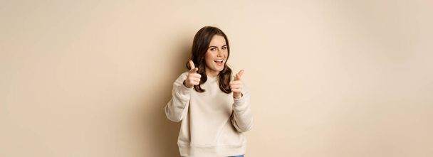 You got this. Happy young woman pointing fingers at camera, praising, complimenting, congrats gesture, standing over beige background. - Foto, Imagem