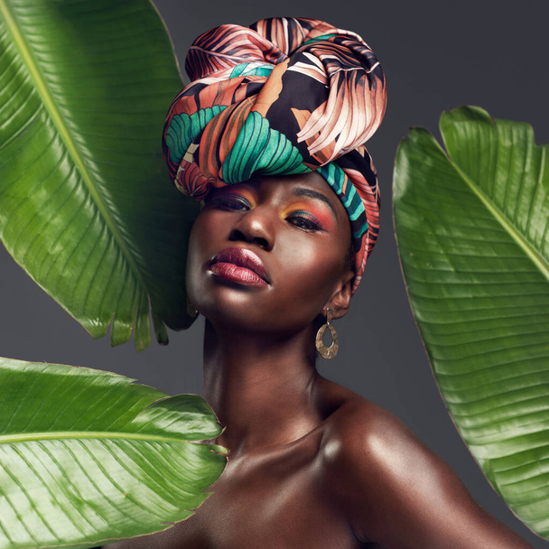 Mějte vlasy přikryté, chraňte je. Studio záběr krásné mladé ženy na sobě tradiční africké hlavy zábal na listnatém pozadí - Fotografie, Obrázek