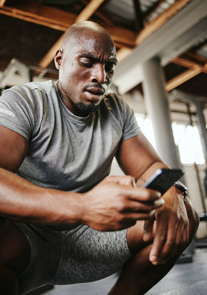 Telefon, fitness és izzadtság egy fekete férfi sportoló ellenőrzi a közösségi média edzés vagy testmozgás után a tornateremben. Képzés, mobil és egészségügyi egy férfi nyomon követi a haladást egy internetes alkalmazás. - Fotó, kép