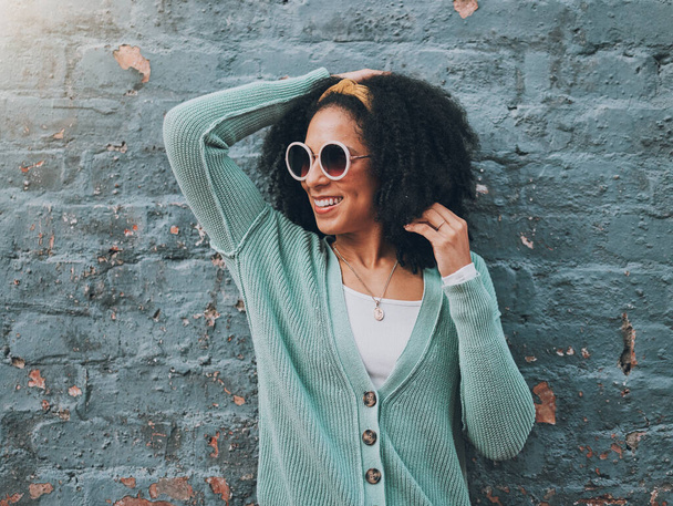 Brazilian woman, fashion and sunglasses by city building wall for fun summer holiday, weekend break or urban vacation. Smile, happy student or afro tourist in trendy, cool clothes and style eye care. - Photo, Image