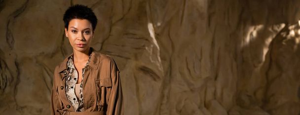 morena arqueólogo en chaqueta marrón mirando a la cámara en la cueva, pancarta - Foto, imagen