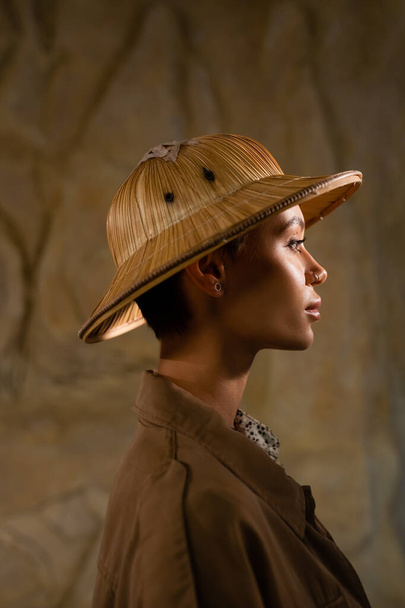 zijaanzicht van archeoloog in safari hoed en bruine jas in woestijn - Foto, afbeelding