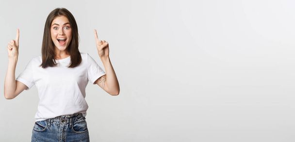 Attractive smiling brunette girl pointing fingers up, showing logo. - Photo, Image