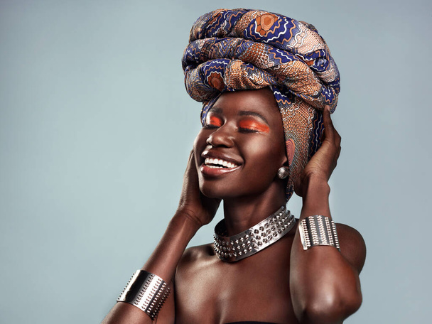 Verberg je erfgoed niet, draag het trots. Studio shot van een mooie jonge vrouw met een traditionele Afrikaanse hoofddoek tegen een grijze achtergrond - Foto, afbeelding