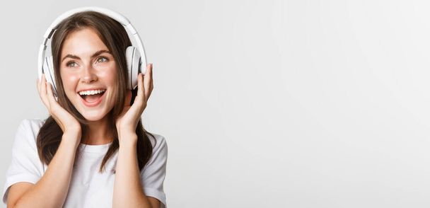 Primer plano de hermosa chica feliz sonriendo, disfrutando escuchando música en auriculares inalámbricos. - Foto, Imagen
