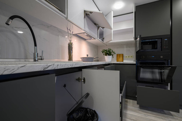 Showcase interior of modern simple dark grey and white kitchen, drawers retracted, doors open - Foto, Bild