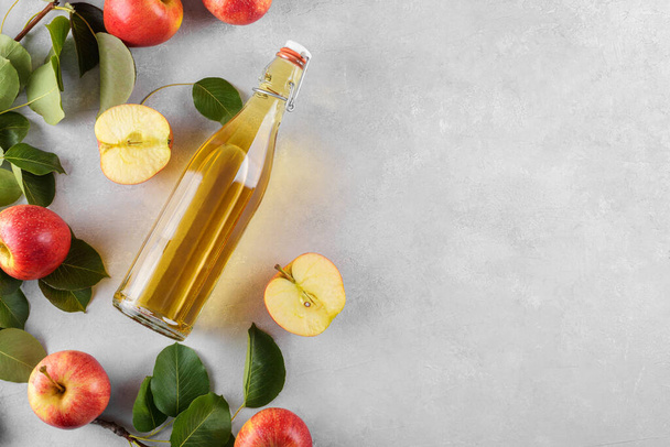 Appelciderazijn van gefermenteerd fruit in een glazen fles met verse biologische rijpe rode appels op een lichte tafelondergrond. Vitamine superfood drank, Gezond eten lifestyle concept, bovenaanzicht, kopieerruimte - Foto, afbeelding