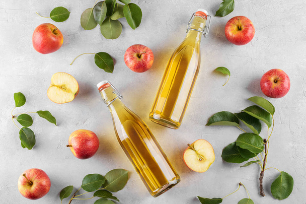 発酵フルーツのアップルサイダー酢は、薄い背景に新鮮な有機熟した赤いリンゴを持つ2つのガラス瓶に入れます。ビタミンスーパーフードドリンク、健康的な食生活のコンセプト、トップビュー、フラットレイアウト - 写真・画像