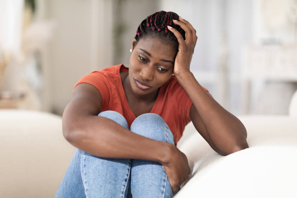 Portret van depressieve jonge zwarte vrouw zit op de bank thuis, Verontrustende Pensive Afro-Amerikaanse vrouw leunend hoofd op de hand en op zoek weg, lijden Mental Breakdown of seizoensgebonden depressie - Foto, afbeelding