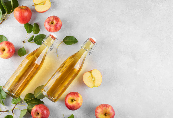 Ocet jabłkowy z fermentowanych owoców w dwie szklane butelki ze świeżymi organicznymi dojrzałymi czerwonymi jabłkami na jasnym tle. Witamina superfood drink, Zdrowe jedzenie koncepcja stylu życia, widok z góry, przestrzeń kopiowania - Zdjęcie, obraz