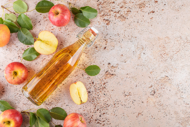 Appelciderazijn van gefermenteerd fruit in een glazen fles met verse biologische rijpe rode appels op beige betonnen ondergrond. Vitamine superfood drank, Gezonde eetstijl, bovenaanzicht, kopieerruimte - Foto, afbeelding