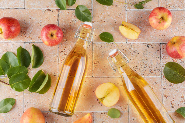 Omenaviinietikkaa fermentoiduista hedelmistä kahteen lasipulloon, joissa on tuoreita orgaanisia kypsiä punaisia omenoita beige-betonitaustalla. Vitamiini superruoka juoma, Terveellinen syöminen elämäntapa, ylhäältä, tasainen lay - Valokuva, kuva