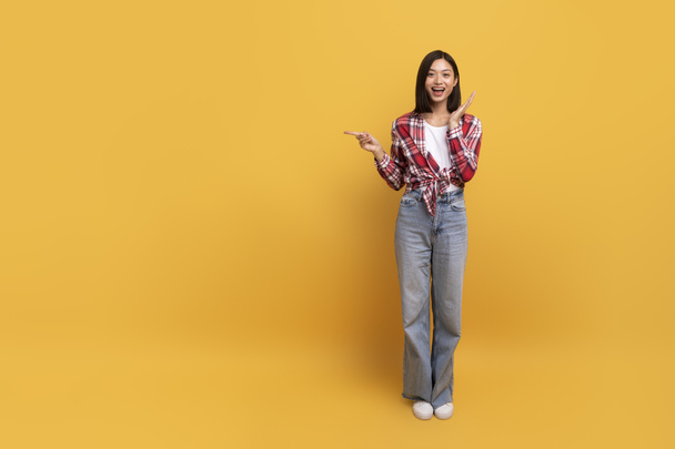 Special offer. Excited korean lady pointing finger aside at copy space standing isolated over yellow studio background, full body length, banner. Positive woman showing place for ad - Fotoğraf, Görsel