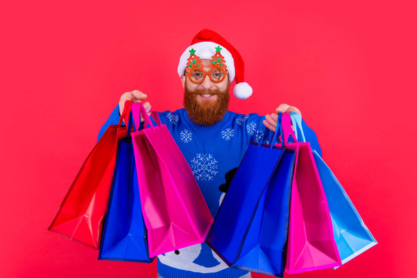 xmas shopping sale. positive man with shopping bag after xmas sale. santa man with xmas shopping bag at sale isolated on red. - 写真・画像
