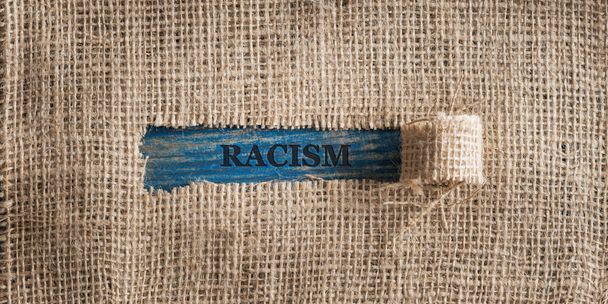 Top kilátás egy durva vászon szövet egy szakadt ablak közepén a szó rasszizmus írt bele. - Fotó, kép