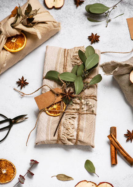 Presente de Natal envolto em pano de linho decorado com paus de canela, maçã seca e fatias de laranja. Furoshiki apresenta. - Foto, Imagem