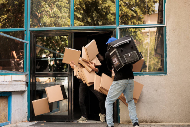 Deliveryman dropping pizza boxes pile at customer, clumsy courier carrying client food order outdoors. Bad delivery service, african american man with falling fastfood packages huge stack - Photo, Image