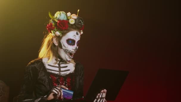 Santa Muerte online vásárol laptopon, hitelkártyával fizet a stúdióban. Elektronikus fizetési tranzakciót bonyolítani PC-n, úgy kinézni, mint a halál istennője Halloweenkor. Kézi lövés.. - Felvétel, videó