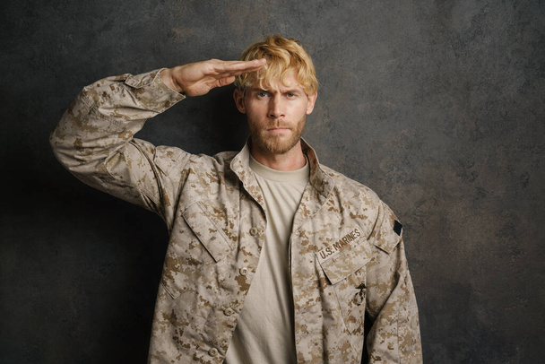 White military man wearing uniform saluting and looking at camera isolated over black background - Фото, изображение