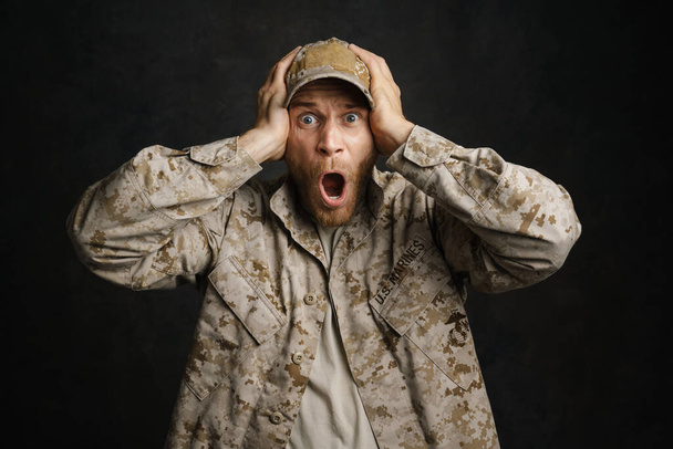 White military man wearing uniform screaming while holding his head isolated over black background - Fotoğraf, Görsel
