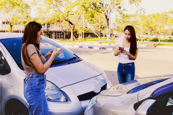 交通ルールを破る車線で車を運転する2人の若い女性は、自動車保険の主張の証拠として一緒に写真を撮るためにスマートフォンを使用しています:事故や自動車保険の概念. - 写真・画像