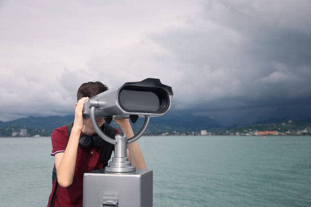 Teenage boy looking through mounted binoculars near sea. Space for text - Valokuva, kuva