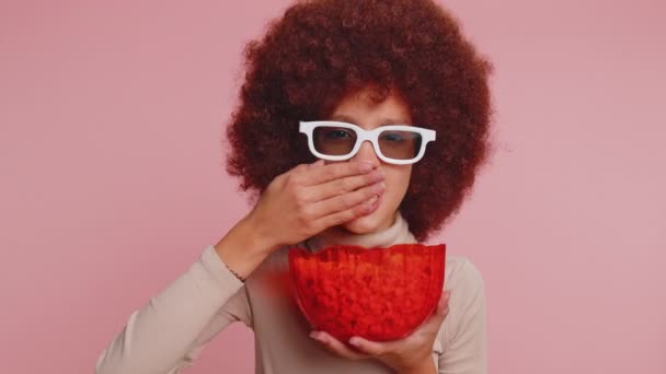Ενθουσιασμένο νεαρό αστείο κορίτσι του σχολείου σε 3D γυαλιά τρώει ποπ κορν, βλέποντας ενδιαφέρουσα τηλεοπτική σειρά, σπορ παιχνίδι, ταινία, σε απευθείας σύνδεση περιεχόμενο ταινία social media. Έφηβος ένα θηλυκό παιδί στο στούντιο ροζ φόντο - Πλάνα, βίντεο