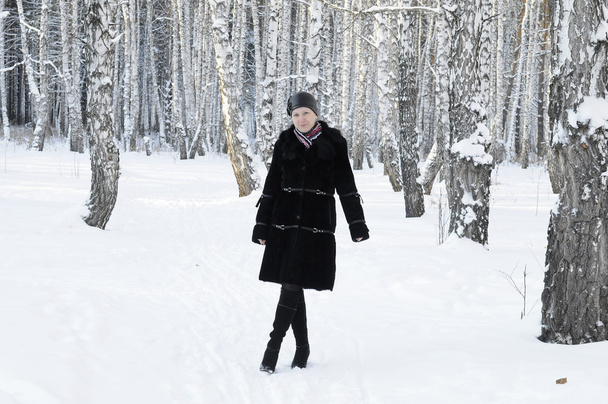 The woman in a black fur coat costs in the birch wood in the win - Fotó, kép