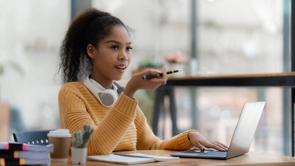 Retrato de una hermosa mujer negra joven usando el ordenador portátil en la cafetería. - Foto, Imagen
