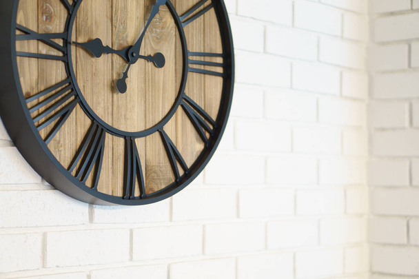 Relógio de madeira com mãos pretas e números colocados no papel de parede branco com design de tijolo - Foto, Imagem