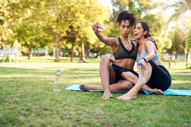 Zabawna mina. Full length shot dwóch atrakcyjnych młodych kobiet pozowanie do selfie podczas pobytu w parku w ciągu dnia - Zdjęcie, obraz