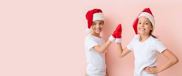 Heureux petits enfants dans chapeaux de Père Noël donnant high-five les uns aux autres sur fond rose avec de l'espace pour le texte - Photo, image