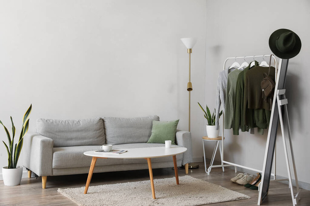 Интерьер светлой гостиной с вешалкой, свитерами и диваном - Фото, изображение