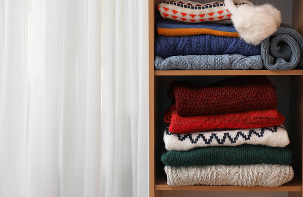 Shelving unit with folded sweaters near light curtain, closeup - Photo, Image