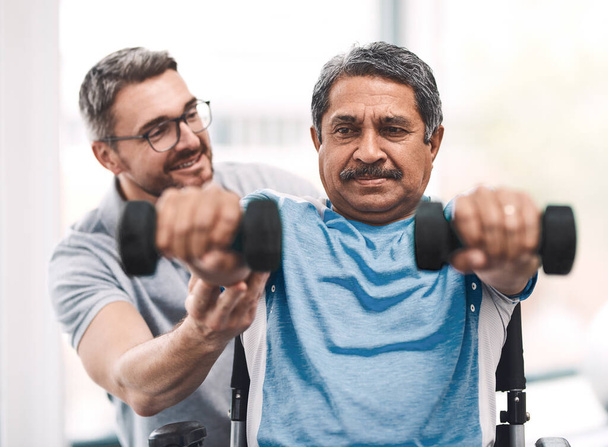 Os resultados já estão a começar a aparecer. um homem idoso se exercitando com halteres durante uma sessão de reabilitação com seu fisioterapeuta - Foto, Imagem