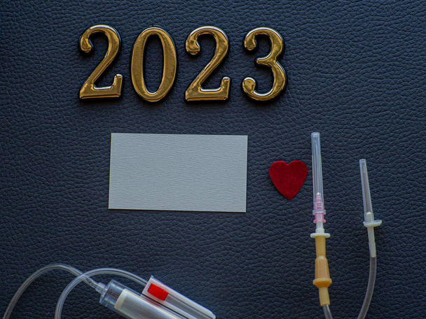 2023, медицина и донорство крови. Крупный план фотографии 2023 года и место для текста на темном фоне. Рождественская медицинская открытка с бумажными красными сердцами, пластиковой внутривенной системой и копировальным пространством.  - Фото, изображение