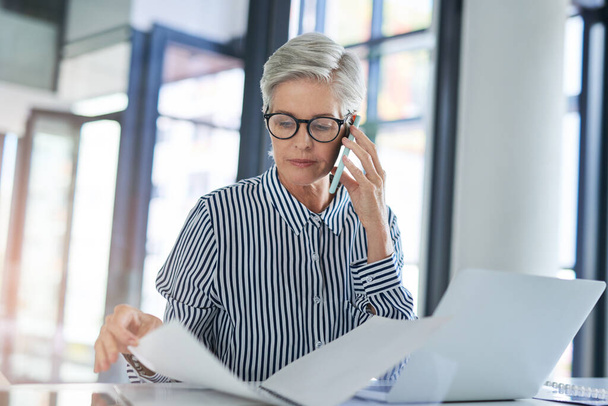 A elfoglalt nők sikeres nőkké válnak. egy vonzó, érett üzletasszony kezeli a papírmunkát, miközben telefonál az irodai asztalánál a munkahelyén. - Fotó, kép