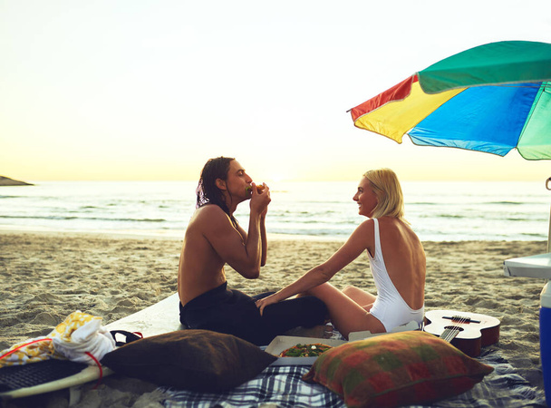 Seeing you comfortable makes me happy. a happy young couple having a picnic date and eating on the beach at sunset - Foto, Imagen