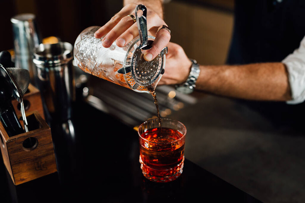 close up of barman pouring cocktail into glass - Фото, зображення