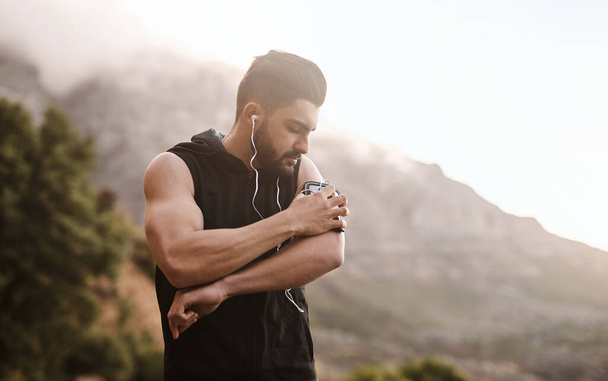 Setting up a heart-pumping playlist. a sporty young man listening to music while exercising outdoors - Photo, Image