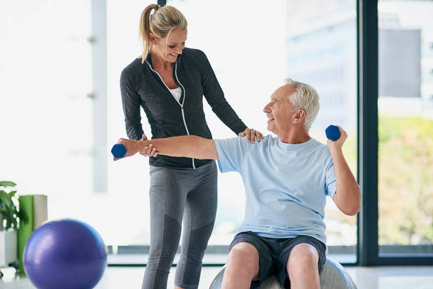 Je spieren worden sterker. een vriendelijke vrouwelijke fysiotherapeut helpen haar senior patiënt uit te werken met gewichten - Foto, afbeelding