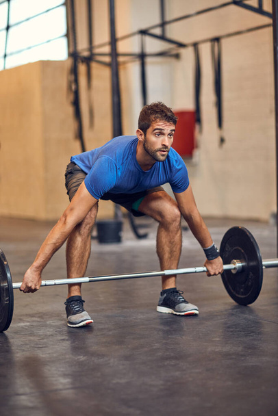 Еще разок. Полнометражный снимок красивого молодого человека, поднимающего тяжести во время тренировки в спортзале - Фото, изображение