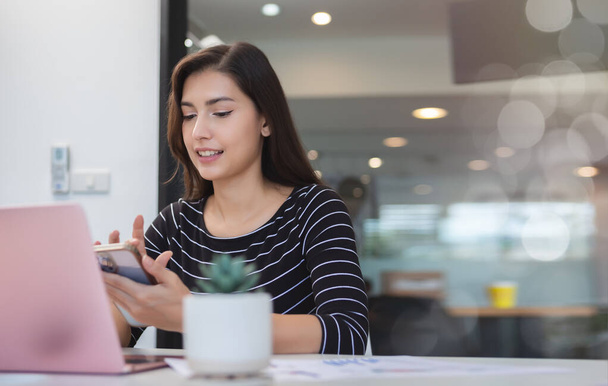 Mujer de negocios asiática usando smartphone y trabajando con laptop. mujer freelance profesional llamando con consultas de trabajo al cliente. - Foto, Imagen