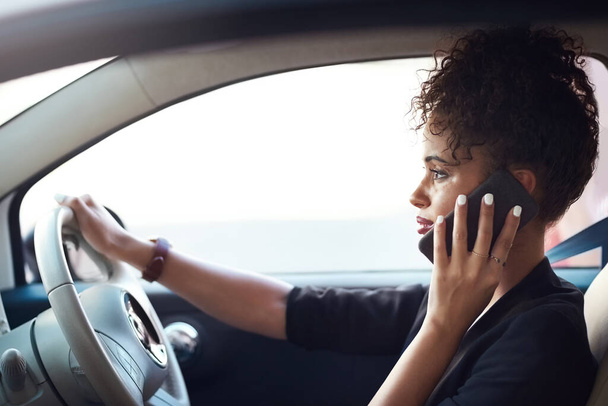 Hacer las cosas en movimiento. una atractiva joven empresaria que toma un teléfono mientras conduce su coche - Foto, imagen