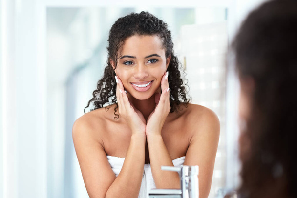 If you want better skin, work for it. a beautiful young woman looking pleased while looking in the bathroom mirror - Foto, imagen
