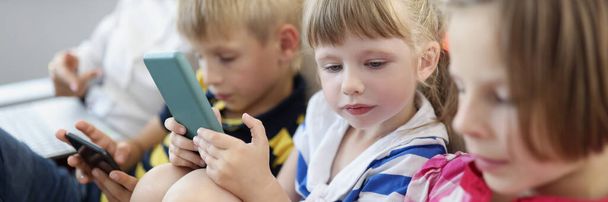 Portrait of children at home, stare at smartphone screens, addiction to modern technologies. Kids use gadgets from young age. Addict, childhood concept - Foto, Bild